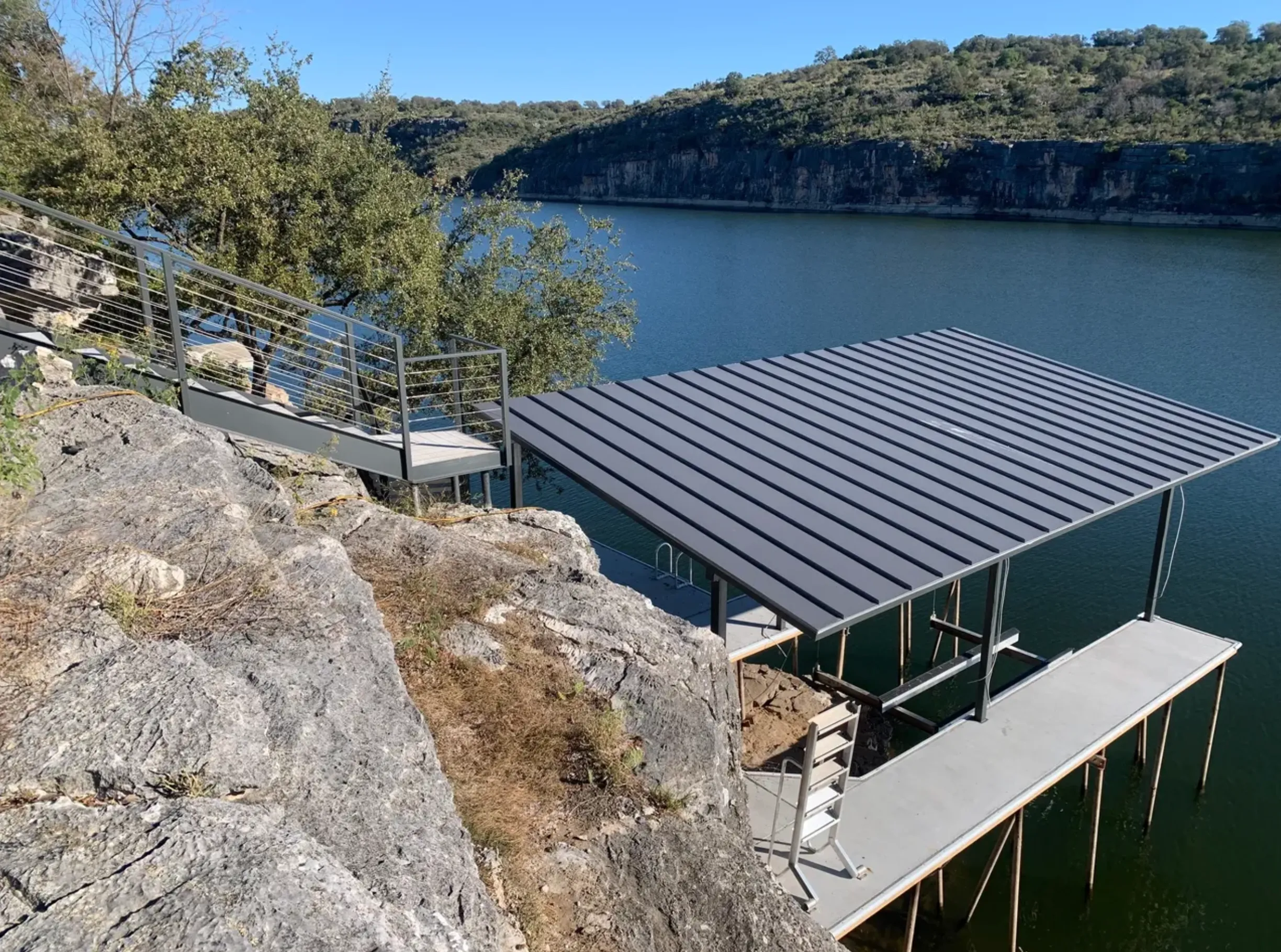 Covered boat dock and steel gangway built below a limestone bluff on a Hill Country lake